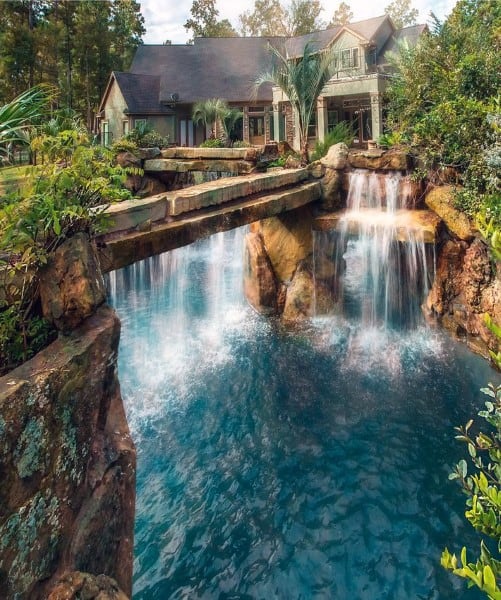 Backyard waterfall with stone bridge and scenic pond near rustic house.