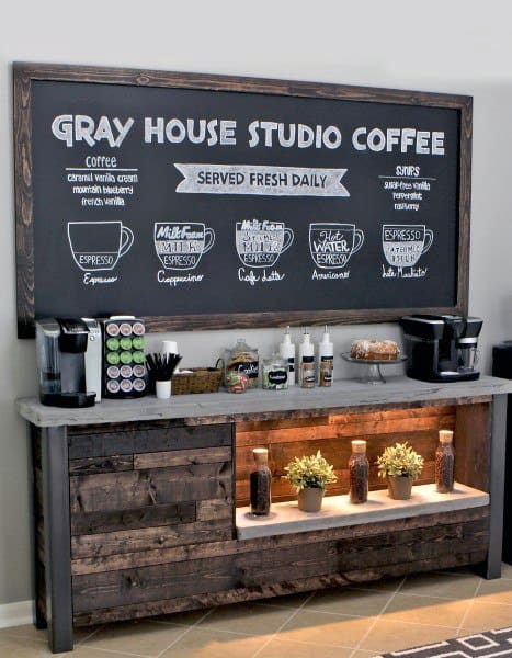 Rustic coffee bar with chalkboard menu, coffee machines, and illuminated shelf with decor.