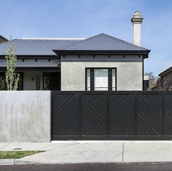 Modern house with black driveway gate and concrete wall featuring minimalist architecture.