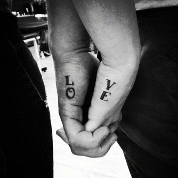 Matching hand tattoos spelling out LOVE across both partners' fingers, visible when holding hands together.