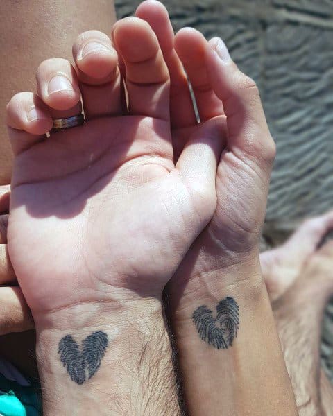 Matching wrist tattoos of heart-shaped fingerprints on a couple, symbolizing love and individuality intertwined.