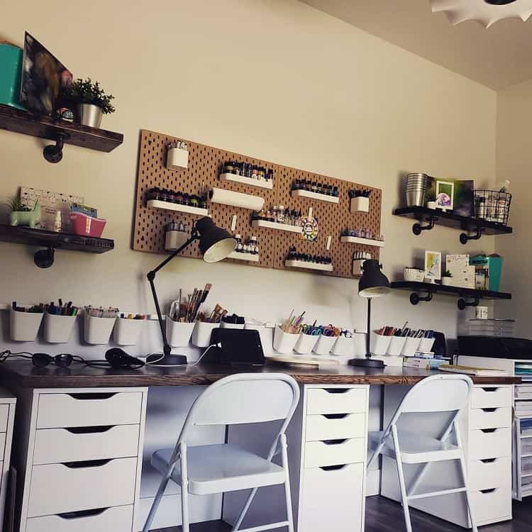 Organized home office with white desks, chairs, lamps, shelves, and craft supplies neatly arranged on a pegboard