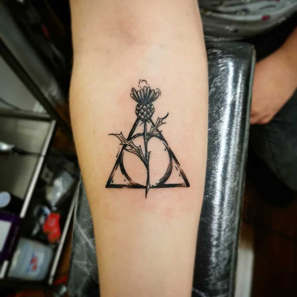 Minimalist Deathly Hallows tattoo with a delicate thistle flower and subtle branch details, blending nature with the magical symbol.