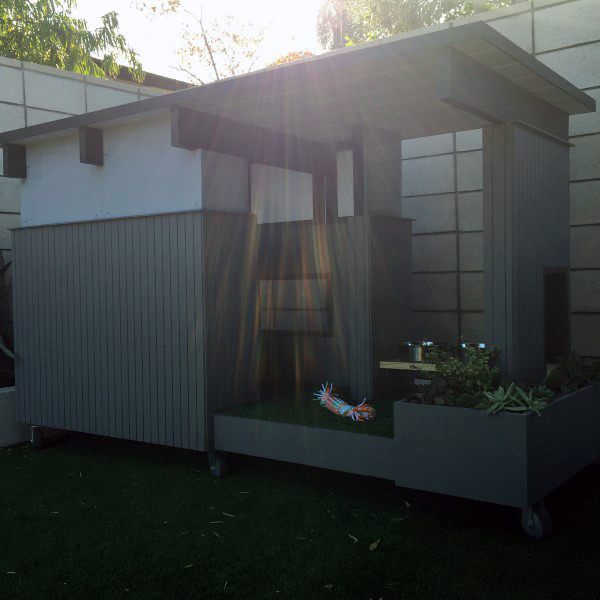 Modern dog house with a sleek, minimalist design featuring a shaded area, rolling base, and plant box, surrounded by grass
