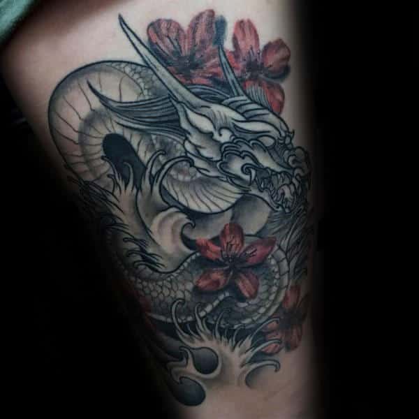 Thigh tattoo featuring a detailed black and grey Japanese dragon with fierce expression, surrounded by bold red cherry blossoms