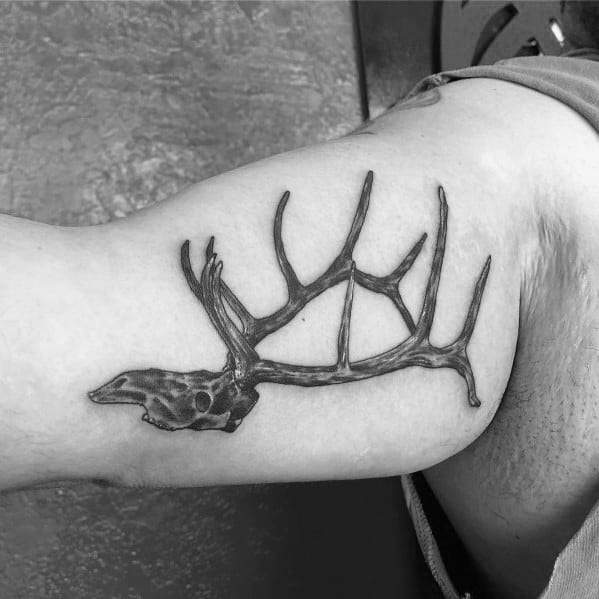 Black and grey elk skull tattoo with large antlers on a man's bicep, featuring fine linework and detailed shading for a bold look.