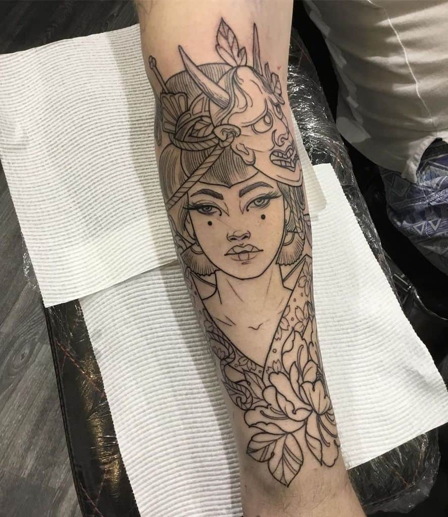 Black linework forearm tattoo of a Geisha with a Hannya mask on her head, floral details, and intricate patterns blending tradition and mysticism.