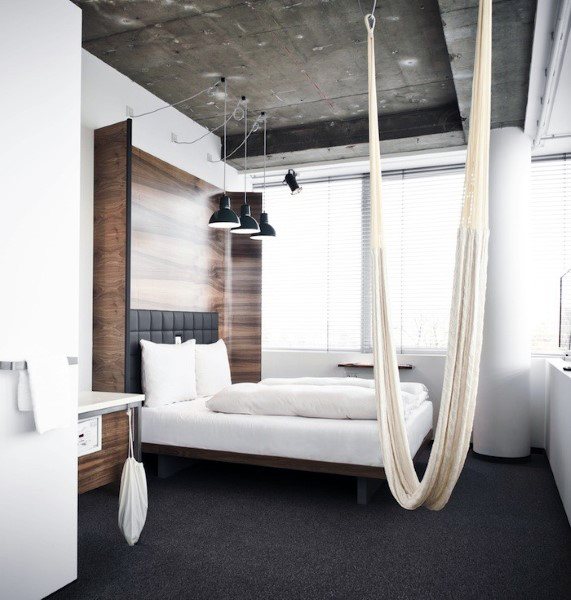 Modern bedroom with a wooden accent wall, cozy bed, and hanging indoor hammock.