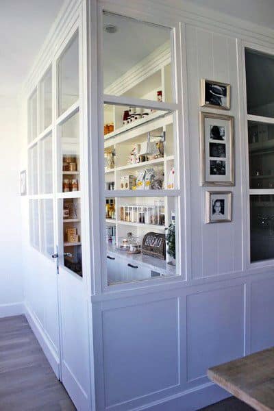 Modern kitchen pantry with glass doors and organized shelves.