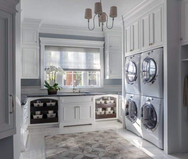Stacked washers and dryers in a bright laundry room with white cabinets and natural light.