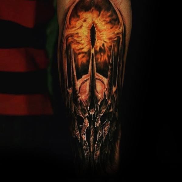 Realistic tattoo of the Eye of Sauron, ablaze with fiery intensity, paired with a spiked helmet on an arm