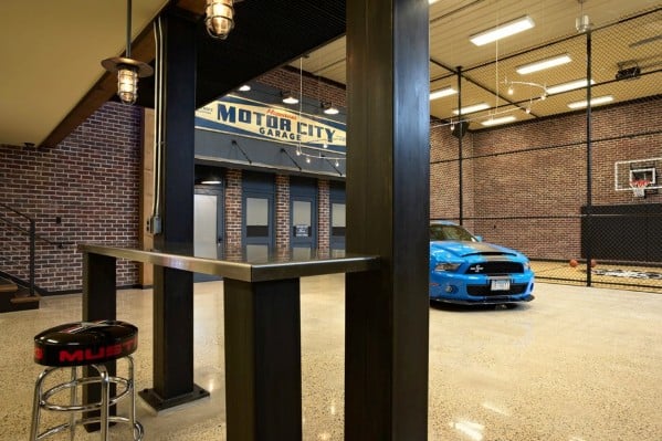 Industrial-style man cave with a blue car, basketball hoop, brick walls, and metal accents