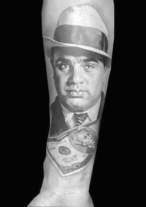 Al Capone tattoo featuring a detailed portrait of the gangster, with his iconic fedora and a dollar bill draped around his neck.