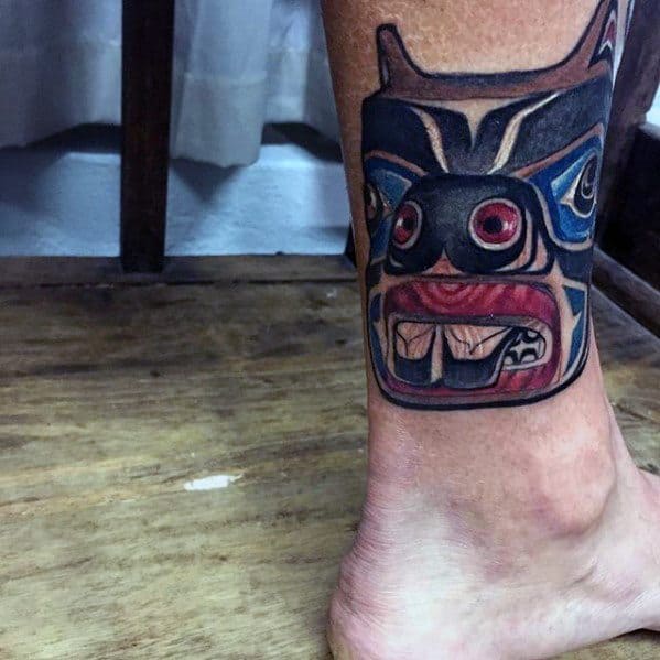 Beaver tattoo on lower leg in bold Native American style with red eyes, sharp teeth, and intricate black and blue patterns.