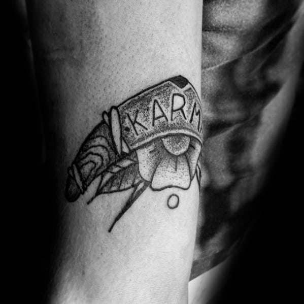 Boomerang tattoo with the word KARMA, combined with a geometric flower and dot detailing on the inner forearm.