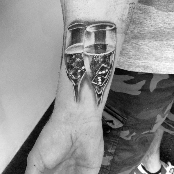 Arm tattoo of two clinking champagne glasses, with detailed bubbles, on a person wearing a camo-patterned garment.