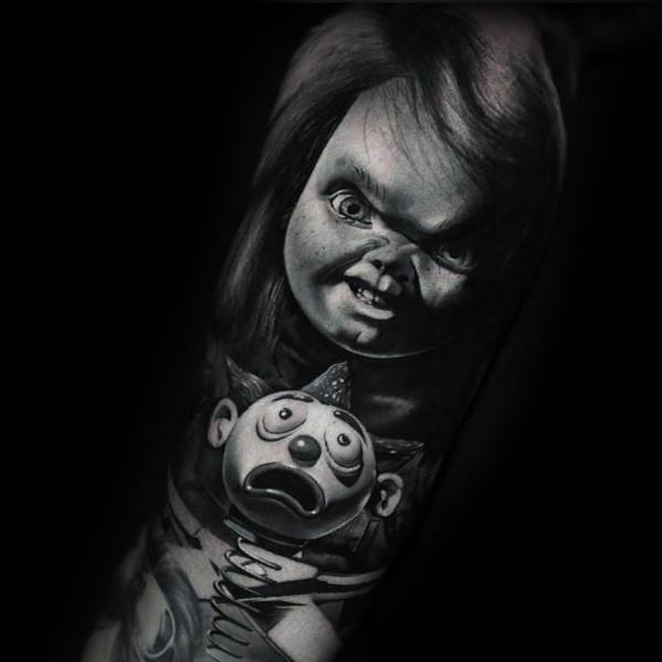 Black and grey Chucky tattoo featuring his eerie grin and intense stare, holding a frightened jack-in-the-box clown for a haunting effect.