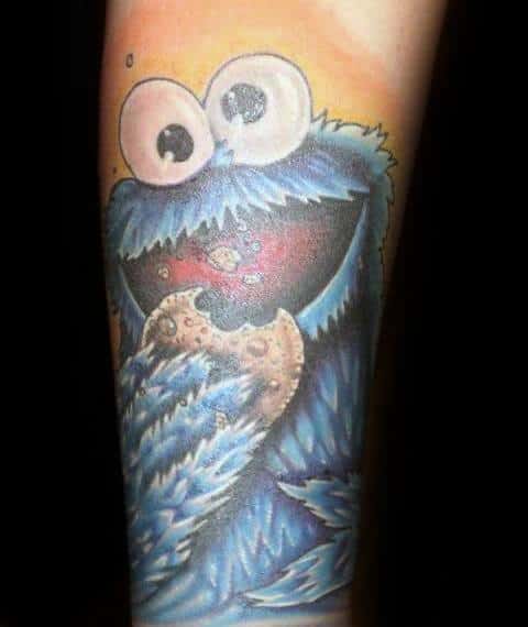 Classic Cookie Monster tattoo with wide eyes and fluffy blue fur, happily munching on a cookie against a warm yellow background.