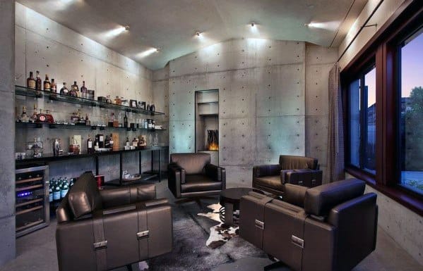 Modern man cave with leather chairs, a glass shelf with bottles, a small table, and a large window with evening light