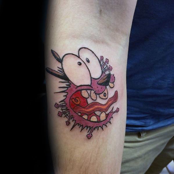 Courage the Cowardly Dog tattoo showing a wild, exaggerated expression with bulging eyes and torn skin effect on the inner forearm.