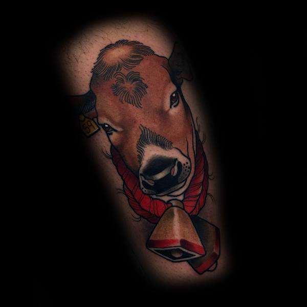 Realistic cow head tattoo with bold outlines, red rope detail, and a bell, shaded with brown and black tones on the arm.