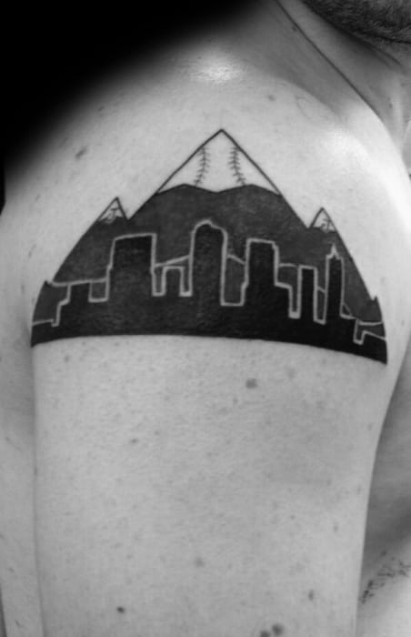 Denver skyline and mountain tattoo on upper arm, featuring bold cityscape silhouette with snowy peaks in the background.