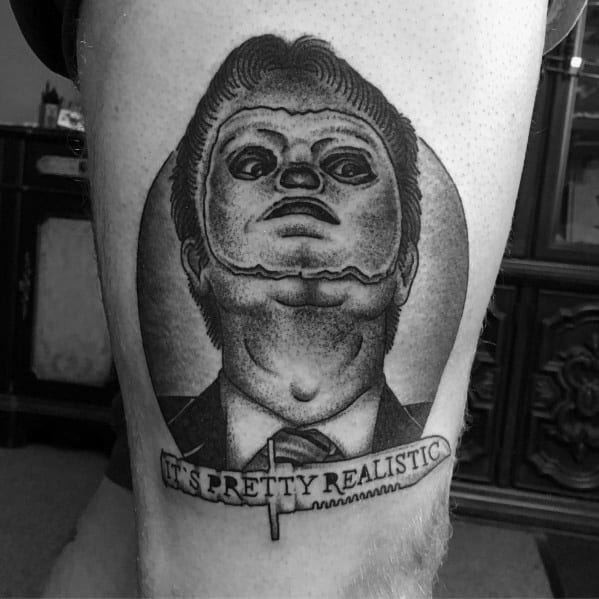 Black and grey tattoo of Dwight Schrute with an exaggerated puppet-like face, captioned It's Pretty Realistic, on a man's leg.