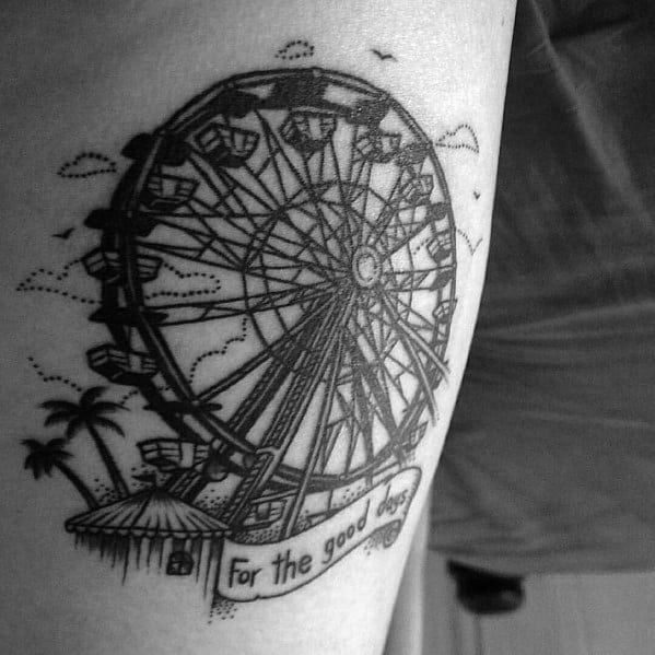 Detailed black ink Ferris wheel tattoo with a banner reading For the good days, palm trees, and birds in the background.