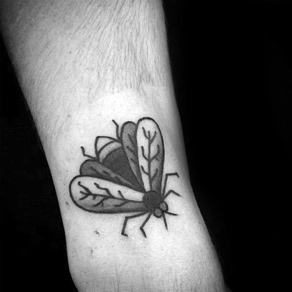 Black ink fly tattoo on forearm with bold outlines and leaf-like wing patterns, giving it a unique graphic style.