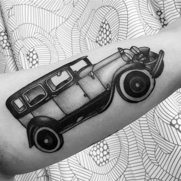 Black and grey vintage Ford tattoo on forearm, showcasing a classic car design with detailed shading and bold outlines.