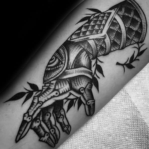 Detailed blackwork tattoo of a mechanical gauntlet with geometric patterns and leafy accents, inked on a man's forearm.