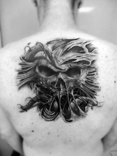 Black and grey back tattoo featuring a demonic skull with flowing, twisted details, creating a dark and surreal gothic design.