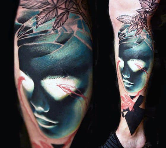 Inverted tattoo of a serene face in dark tones with red accents, geometric shapes, and floral elements on a man's leg.