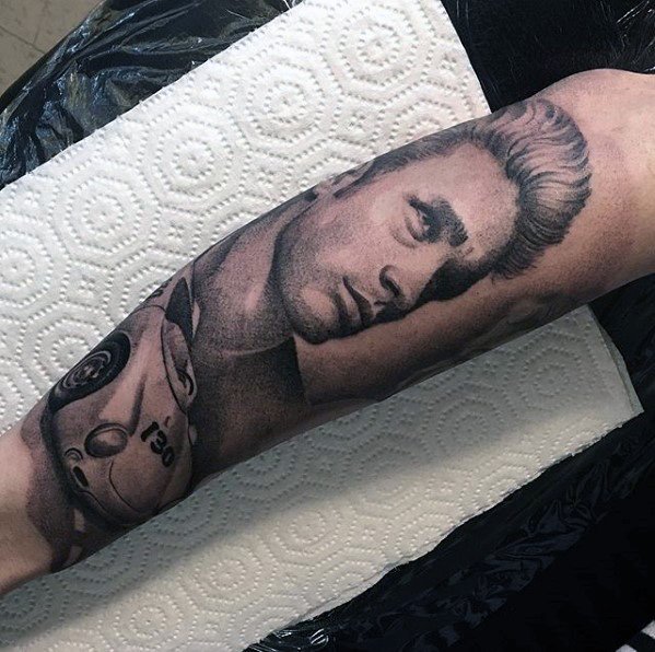 Realistic black and grey tattoo of James Dean’s portrait with his Porsche 550 Spyder on a forearm.