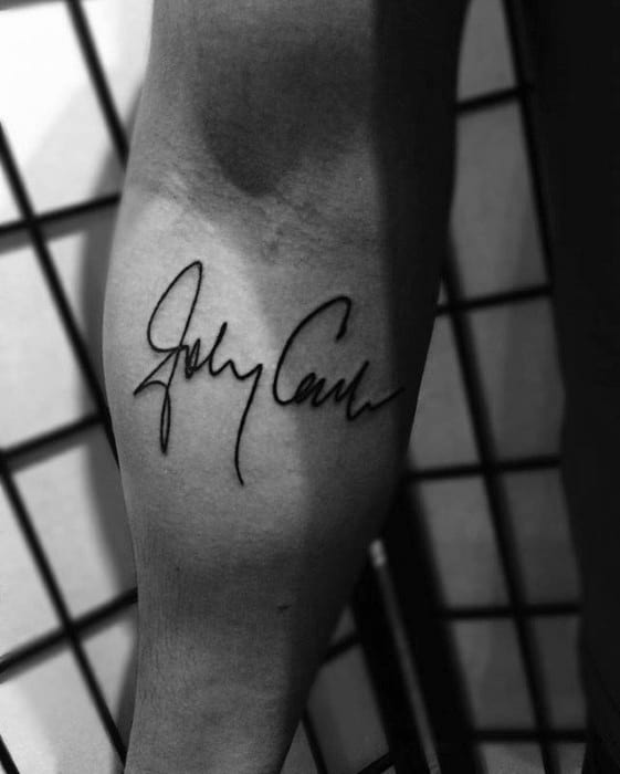 Black tattoo of Johnny Cash's signature on forearm, in a monochrome setting