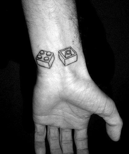 Minimalist Lego block tattoo on wrist, featuring two black-outlined bricks with a 3D effect on the inner forearm.