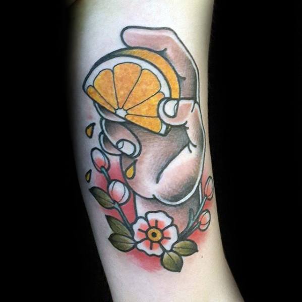 Hand squeezing a lemon slice with juice droplets, surrounded by pink buds and a white flower in a bold, traditional tattoo style.