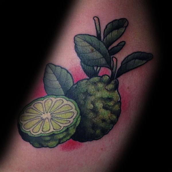 Realistic kaffir lime tattoo with vibrant green hues, detailed leaves, and a sliced lime half, creating a bold and organic design.