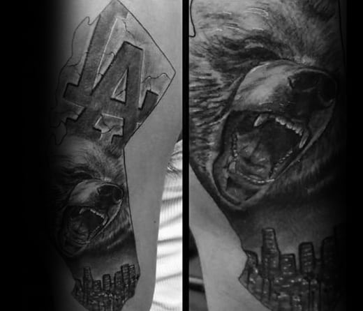 Roaring bear tattoo with LA logo and Los Angeles skyline in black and gray ink on upper arm.