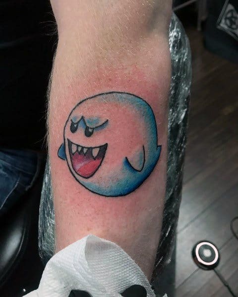 Mario ghost tattoo featuring Boo with a mischievous grin, shaded in blue and black, inked on the forearm with a bold outline.