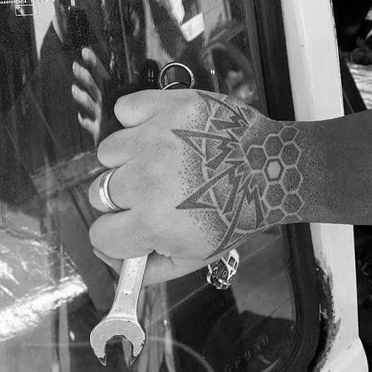 Geometric hand tattoo blending the Metallica ninja star logo with hexagonal patterns, creating a modern, detailed design across the knuckles and wrist.