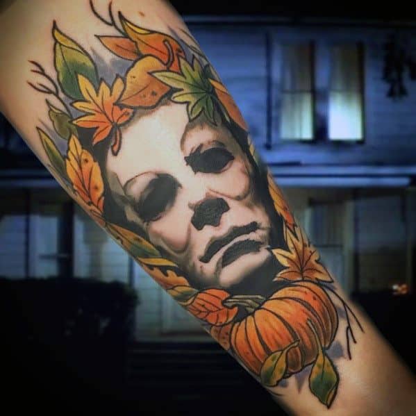 Michael Myers tattoo surrounded by autumn leaves and a pumpkin, blending horror with a seasonal Halloween theme.