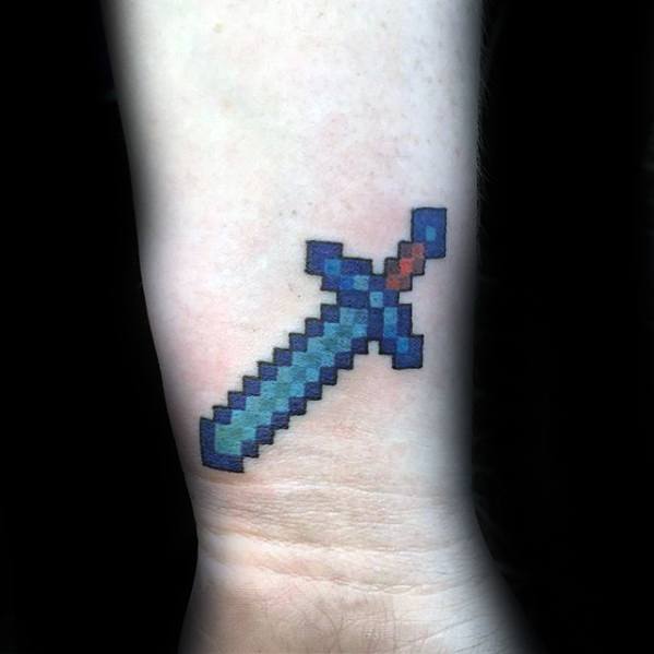 Minecraft pixelated diamond sword tattoo on the inner forearm, designed in bold blue and black tones with red accent details.