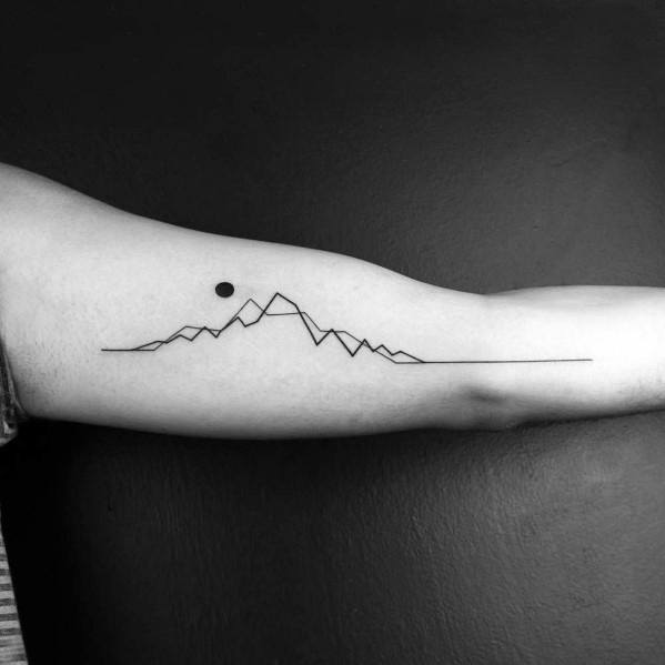 Minimalist mountain tattoo on the inner forearm, featuring a thin line forming peaks with a small dot resembling the sun or moon.