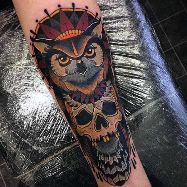 Neo-traditional owl tattoo with bold colors, fierce gaze, and a skull below, featuring intricate shading and geometric details.