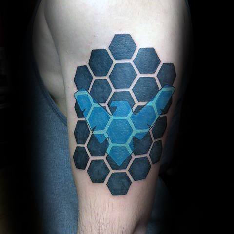 Nightwing tattoo with a bold blue emblem breaking through black hexagonal patterns on the upper arm.