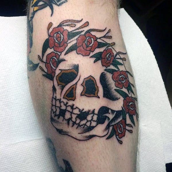 Traditional-style Grateful Dead skull tattoo with a crown of red roses and bold black outlines on the calf.