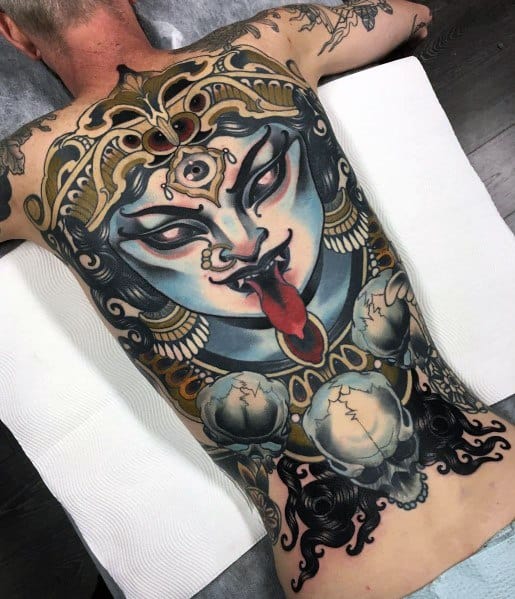 Large full-back tattoo of the Hindu goddess Kali, featuring a fierce expression, blue skin, a third eye, extended tongue, and severed heads.