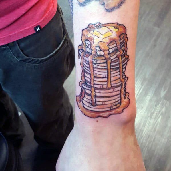 Stack of pancakes tattoo with syrup and butter on a man's forearm, featuring bold outlines and vibrant shading for a realistic look.