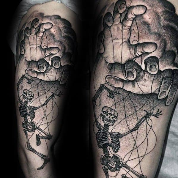 Realistic puppet tattoo of a skeleton controlled by large hands above, detailed with strings and dramatic shading on the arm.
